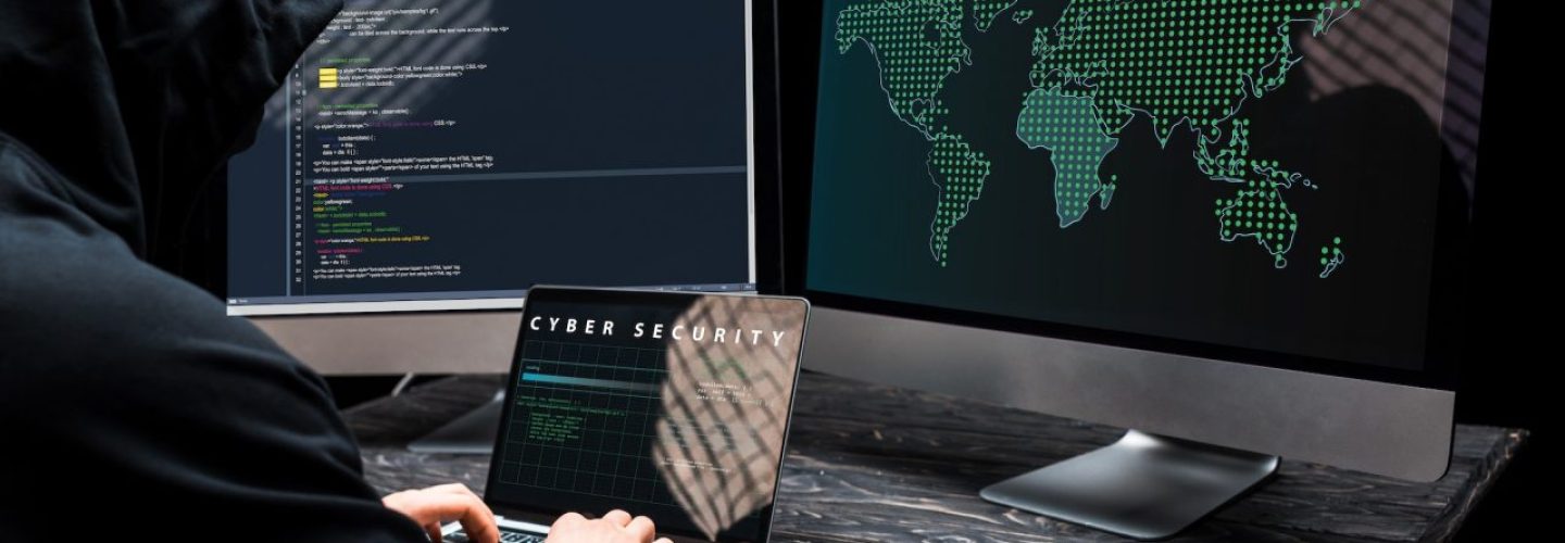 hacker-using-laptop-with-cyber-security-lettering-on-screen-near-computer-monitors-on-black.jpg